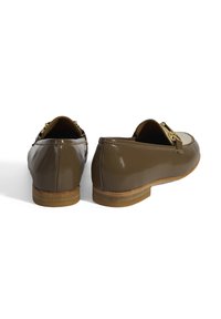 Bruine gepatineerde leren instappers met een lage hak, voorzien van een gouden metalen accent aan de voorkant en een gestructureerde zool. Overal een gladde afwerking.