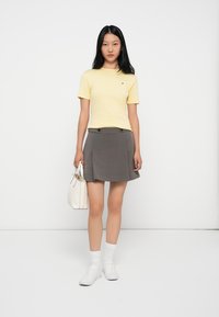 Gul stripete bomull t-skjorte med korte ermer, kombinert med en grå A-linje skjørt med frontknapper, hvite sneakers og en liten hvit veske.