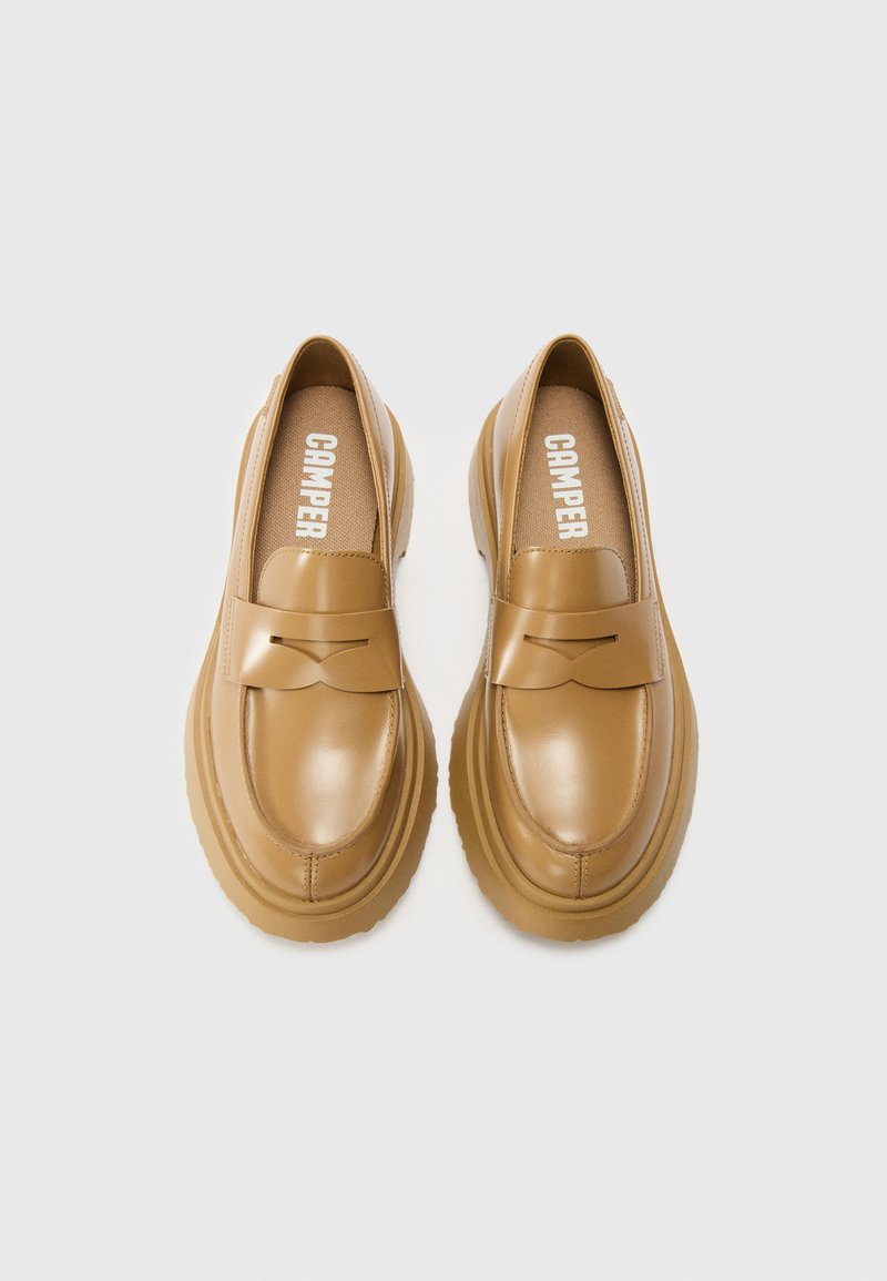 Mocasines de cuero marrón con forma redondeada, diseño cosido y acento de lazo. Logo blanco "CAMPER" en la planta. Suela gruesa y texturizada.