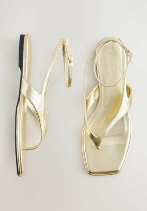 Zlatne metalik sandale s ravnim potplatom, koje imaju moderan dizajn, ukrižene trake i podesivu kopču. Kvadratni oblik prstiju.