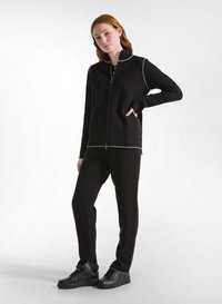 Zwarte zip-up jack met een hoge kraag en contrasterende witte stiksels, gecombineerd met zwarte taps toelopende broek en zwarte sneakers.