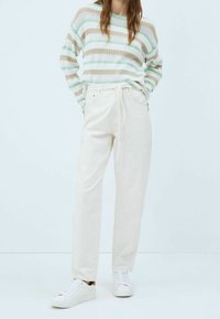 Hvide bomuldsbukser med lige ben, parret med en stribet striktrøje i grøn, beige og hvid. Hvide sneakers bæres.