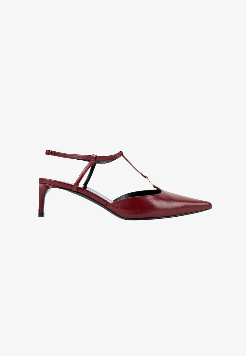 Escarpin slingback en cuir rouge à bout pointu avec bride en T et accent doré sur fond blanc.