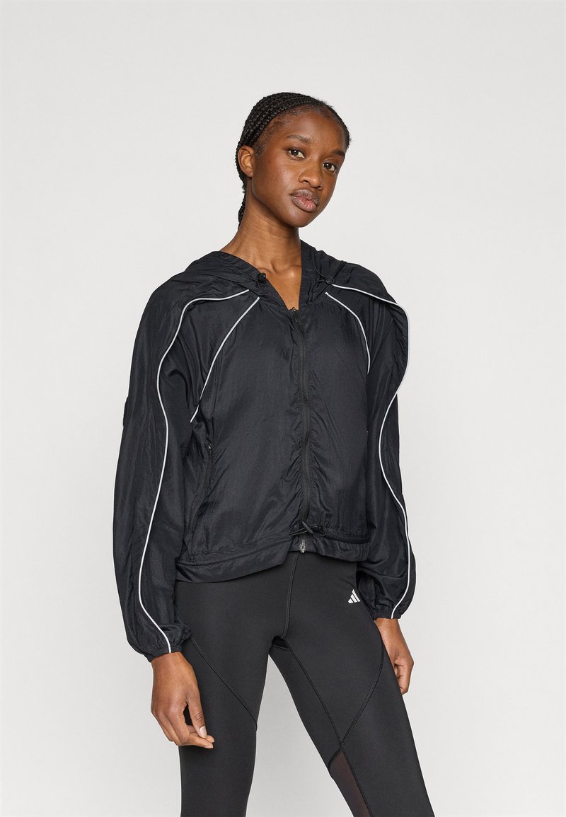 Μαύρο ελαφρύ μπουφάν με κουκούλα, ελαστικές μανσέτες και αντανακλαστικές λευκές λεπτομέρειες περιμετρικά. Διαθέτει φερμουάρ μπροστά και ελαφρώς κοντό μήκος.