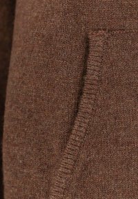 Maglia marrone lavorata a maglia con un disegno strutturato e una tasca laterale visibile. La trama è morbida e presenta una tonalità ricca e calda.