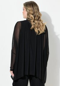 Kimono trasparente nero con maniche fluide, vestibilità ampia e texture leggera, che scende fino alla vita.