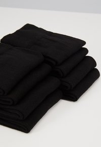 Chaussettes en coton noires empilées soigneusement, mettant en avant une texture douce et une finition lisse. Chaque paire présente un poignet côtelé et une forme uniforme.