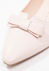 Vaaleanpunaiset kärkitossut, joissa on reikäkuitu, ja etuosassa suuri, sileä nauha, sekä hienovarainen beige pohja.