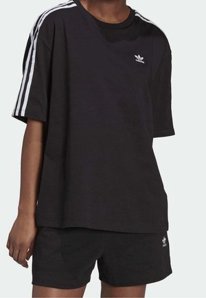 Černé bavlněné tričko s volným střihem, zdobené bílým logem Adidas a třemi svislými pruhy na každém rameni. Nošeno s černými šortkami stejné značky.