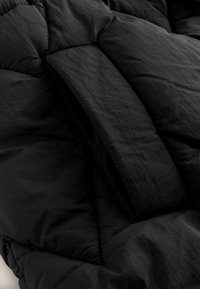 Mustast lõhnavast jope pluusiga, kus on nähtavad õmblused, pehme matt tekstuur ja tõmblukuga taskuava.