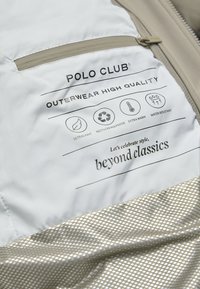 Tessuto esterno di color argento chiaro con una texture liscia. Le caratteristiche includono una cerniera beige, loghi e istruzioni per la cura su un'etichetta bianca.