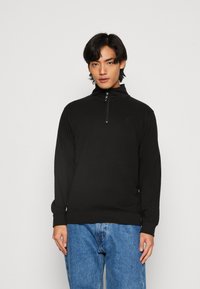 Sort quarter-zip pullover sweatshirt med lange ærmer, ribbede manchetter og bund; glat tekstur; subtilt logo-detalje på brystet.