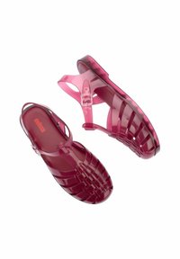 Przezroczyste, jagodowe sandały z żelatyny o plecionej konstrukcji, z regulowanym paskiem na kostkę i okrągłym noskiem. Gładka, błyszcząca textura.