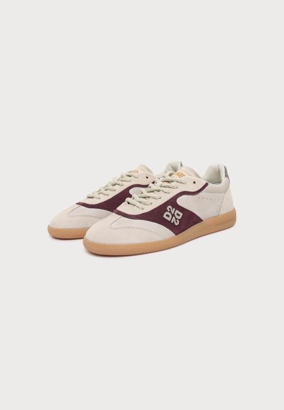 Paire de baskets beige et bordeaux avec semelles en gomme, design à lacets et logo blanc sur le côté, présentées sur un fond blanc uni.