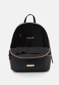 Zaino nero con accessori dorati, chiusura a zip e un ampio scomparto interno. Presenta una piccola tasca con zip e una fodera in tessuto.