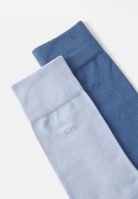 Due paia di calzini: uno blu chiaro e uno blu scuro, entrambi con polsini a coste e una texture liscia, con un logo sottile sul lato.