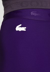 Leggings deportivos morados con una textura suave, que presentan un logo de cocodrilo blanco de Lacoste y una cinturilla con logo tonal.