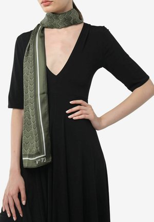 Écharpe verte à motif avec une finition satinée, présentant un design géométrique et un liseré blanc, portée autour du cou sur une robe noire.