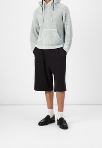 Sudadera de punto azul claro con bolsillo frontal y capucha ajustable, combinada con pantalones cortos negros hasta la rodilla y mocasines negros, usados con calcetines blancos.
