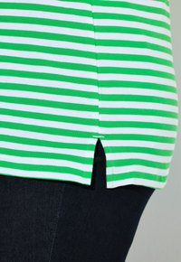 Camicia a righe verdi e bianche con un dettaglio a sfianco, realizzata in un tessuto testurizzato. Abbinata a jeans scuri, con un design slim.