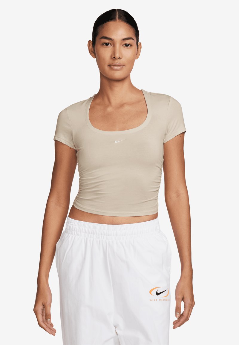 Beige, rövid ujjas, testhezálló crop top, kerek nyakkivágással. A mellkasán egy kis fehér Nike logó található. Puha, rugalmas anyag.