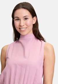 Mouwloze roze top met een hoge hals, zachte stoftextuur en een relaxte pasvorm, die het minimalistische ontwerp en subtiele details benadrukt.