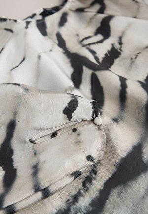 Jedwabna bluzka z monochromatycznym, abstrakcyjnym wzorem w kolorach białym, czarnym i szarym; posiada kieszeń na piersi z zapięciem na guzik oraz gładką fakturę.