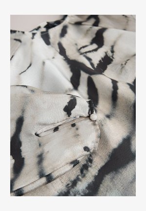 Jedwabna bluzka z monochromatycznym, abstrakcyjnym wzorem w kolorach białym, czarnym i szarym; posiada kieszeń na piersi z zapięciem na guzik oraz gładką fakturę.