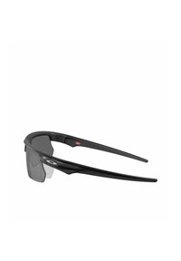 Gafas de sol deportivas negras con un diseño elegante, montura envolvente y lentes grises tintados. Presentan un detalle de logo en el lateral y una forma aerodinámica.