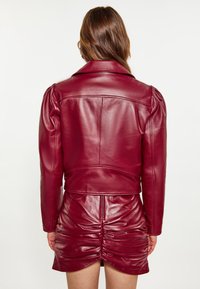 Bordeauxrode leren jas met een gestructureerde kraag, opgeblazen mouwen en naaddetails, gecombineerd met een geplooide leren minirok.