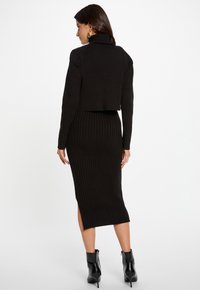 Completo in maglia nera composto da un maglione corto a dolcevita e una gonna midi a costine con spacco laterale, abbinato a stivaletti neri alla caviglia.