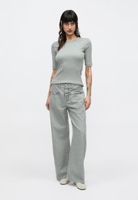 Γκρι τοπ με κοντά μανίκια συνδυασμένο με γκρι τζιν παντελόνι ψηλόμεσο, φαρδύ. Το σύνολο έχει ομαλή υφή και μινιμαλιστικό σχεδιασμό, με ανοιχτόχρωμα παπούτσια.