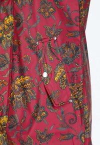 Tela roja con patrón floral y de mariposas en naranja y negro, con un bolsillo rectangular con botones a presión plateados.