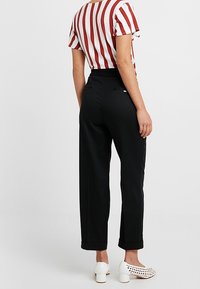 Černé tapered kalhoty se staženým pasem, bočními kapsami a ohrnutými nohavicemi, kombinované s červeno-bílým pruhovaným topem s krátkým rukávem.