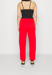 Röda, löst sittande sweatpants med elastisk midja, tillsammans med svarta och vita sneakers med orange detaljer. Enkelt, otexturerat tyg.