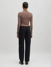 Enganliegende braune Langarmbluse, kombiniert mit dunkelblauen, weit geschnittenen Jeans, die über Gesäßtaschen und eine lockere Silhouette verfügt. Glatte Stofftextur.