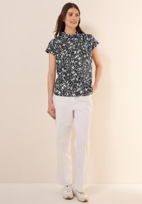 Korte mouw blouse in zwart-wit print, met een kraaghalslijn. Gepaard met witte rechte broek en witte sneakers.