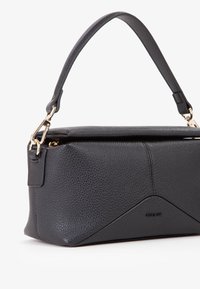 Borsa a tracolla in pelle nera con texture a granuli, design angolare, manico corto e accessori in tono oro. Presenta una chiusura con zip e dettagli del logo.