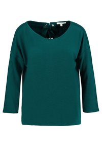 Teal oversized tröja med trekvartsärmar, texturerad tyg, bred halsringning och en knytning i ryggen med metallaccenter.