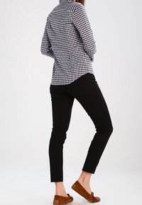 Camicia a quadri bianco e nero, pantaloni neri aderenti e mocassini in suede marrone. Tessuto liscio, vestibilità su misura e dettagli del motivo sottili.