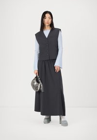 Dark grey waistcoat with large shoulder design, blue ribbed long-sleeve top, flowing dark grey skirt, silver handbag, and light blue platform shoes.