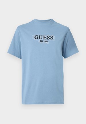 Ljusblå bomulls t-shirt med rund halsringning och korta ärmar, med en tryckt "GUESS EST. 1981" logotyp på framsidan i svart och vitt.