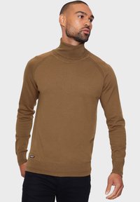 Bruine coltrui met ribbelmanchetten en -zoom, met een gladde textuur en raglan-mouwen. Gecombineerd met donkere broek.