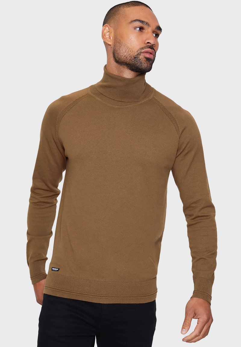 Bruine coltrui met ribbelmanchetten en -zoom, met een gladde textuur en raglan-mouwen. Gecombineerd met donkere broek.