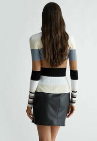 Maglione multicolore a coste con strisce beige, blu, bianche e nere; abbinato a una mini gonna in pelle nera; texture liscia.