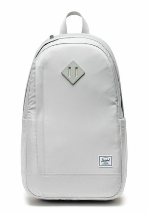 Sac à dos Herschel gris clair avec patch en forme de losange à l'avant, poignée supérieure, compartiment principal zippé et étiquette de marque en bas à droite.