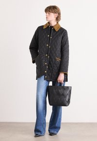 Quilted black jacket with gold hardware, brown corduroy collar, and side pockets. Paired with light denim flared jeans and a black tote bag.
