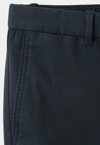 Gros plan sur la ceinture d’un pantalon noir avec passants de ceinture et couture verticale de poche latérale visible sur le côté gauche.