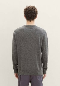 Pull en tricot gris à manches longues, col rond et ourlet côtelé. Le tissu texturé présente un motif subtil. Design minimaliste.