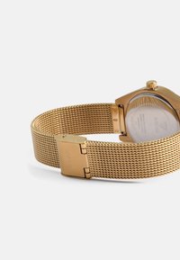 Gold mesh watch band with a secure clasp, featuring a round case, visible movements through a glass back, and textured surface detail.